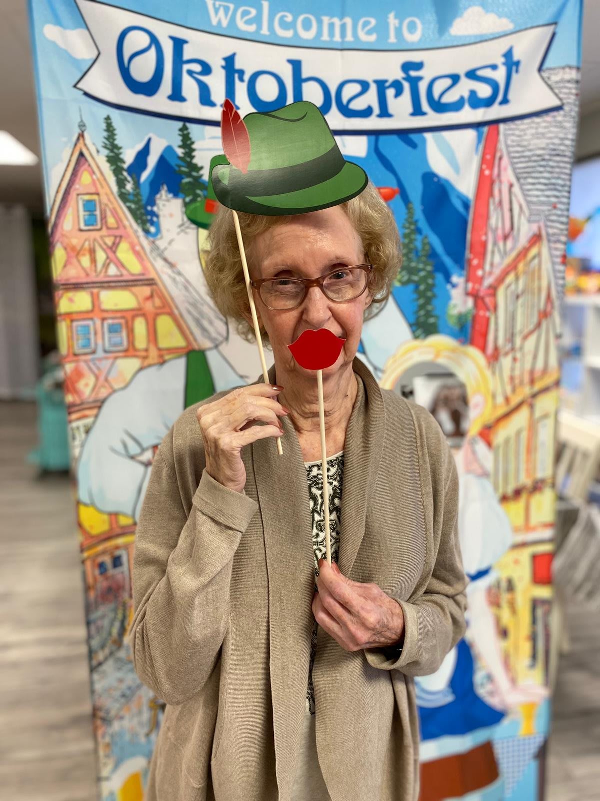 A woman playfully poses with a hat and red nose prop in front of a festive backdrop.