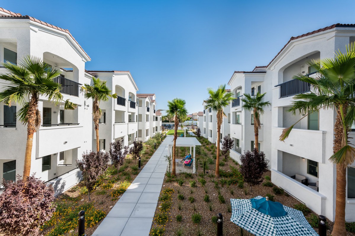 A modern apartment complex with landscaped walkways and palm trees.