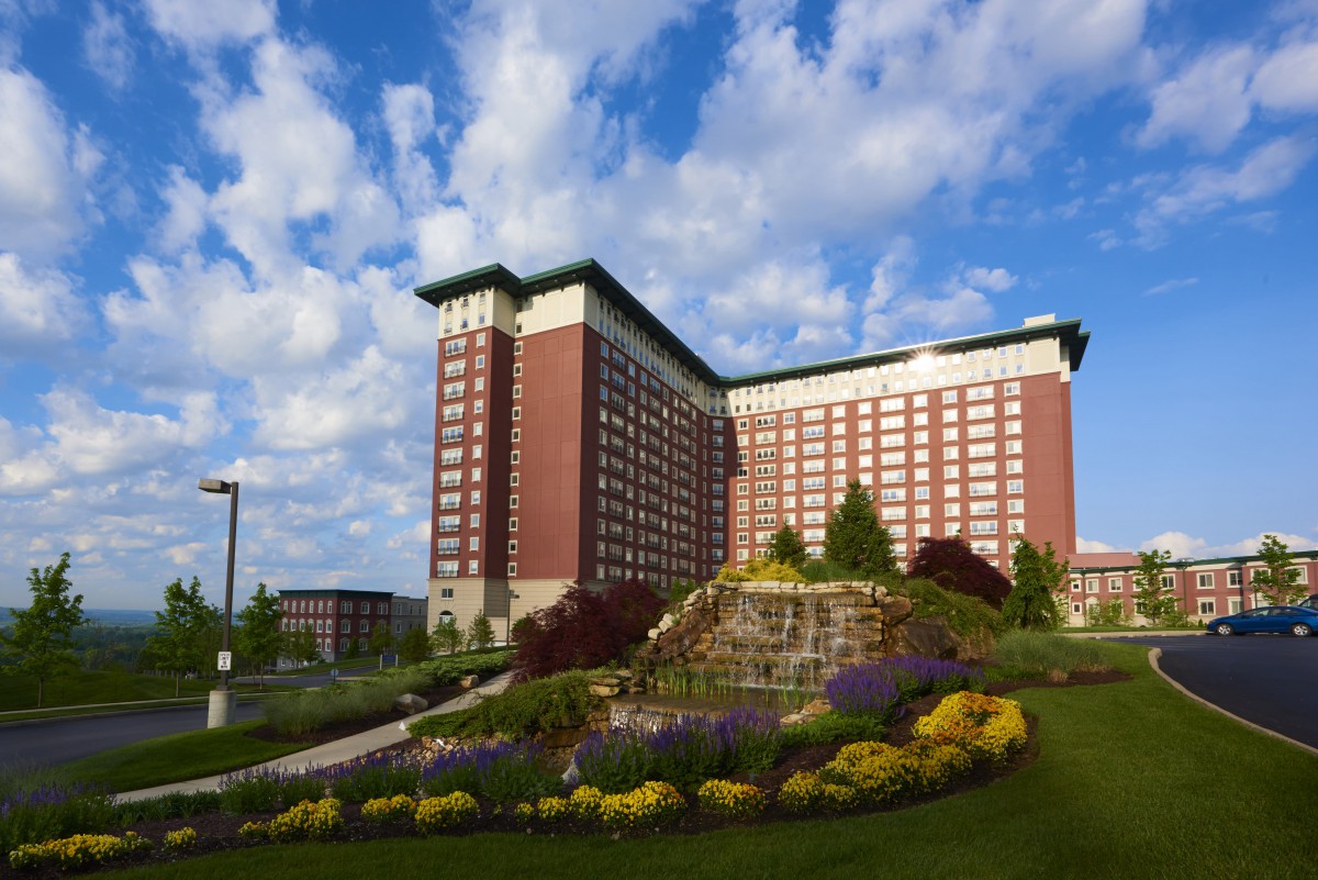 A tall hotel building with well-maintained gardens and vibrant flowers under a partly cloudy sky.