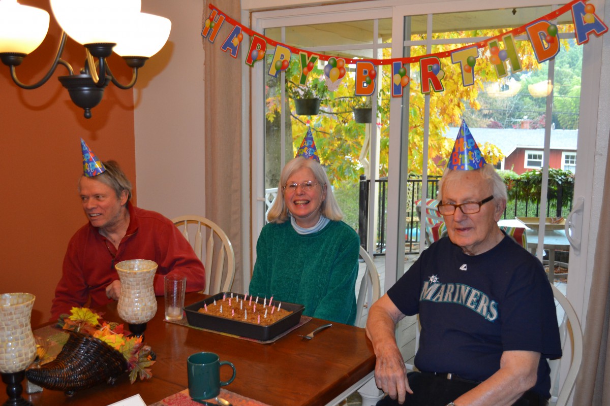 A joyful birthday celebration with three people wearing party hats around a table with a cake.