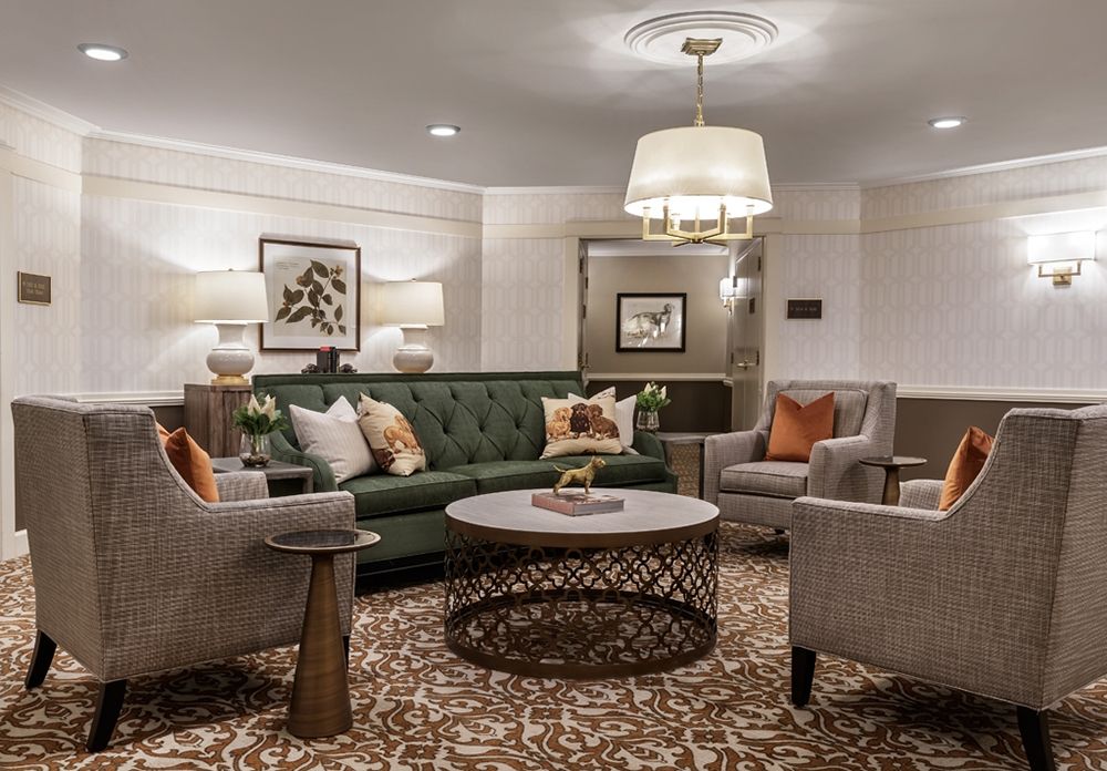 A stylish living room with a green sofa, elegant armchairs, and a decorative coffee table under a chandelier.