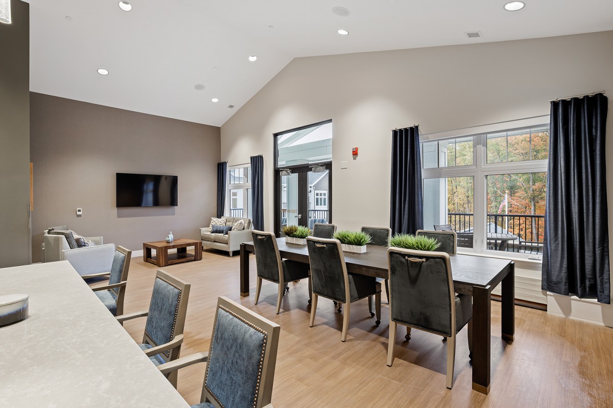 A modern conference room featuring tables, chairs, a television, and large windows with natural light.