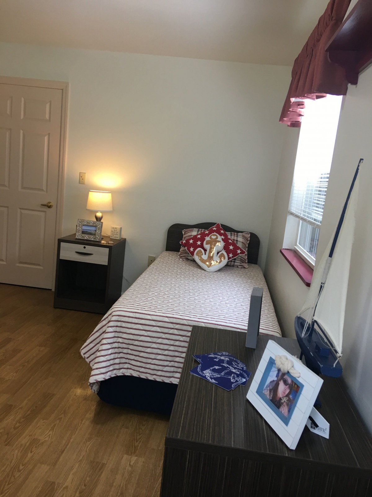 A cozy bedroom with a single bed, nightstand, and a lamp near the window.