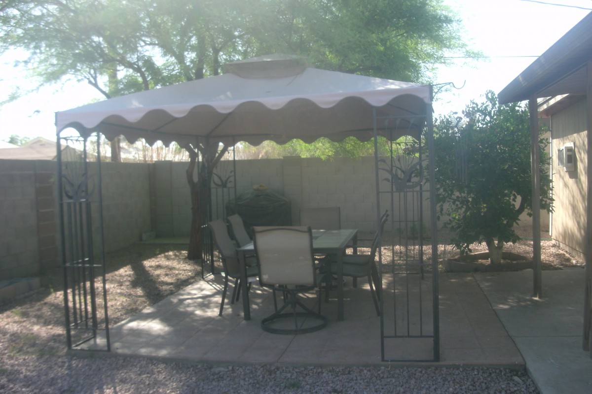 A backyard patio setup with a canopy and outdoor furniture for shaded seating.