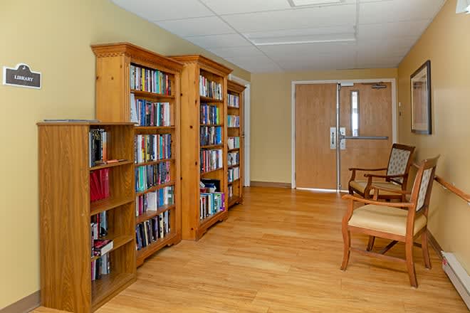 A cozy library room with wooden bookshelves filled with books and a chair on a wooden floor.