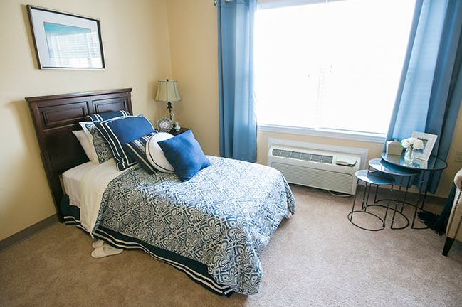 A cozy bedroom with a neatly made bed, blue and white bedding, and a window with blue curtains.