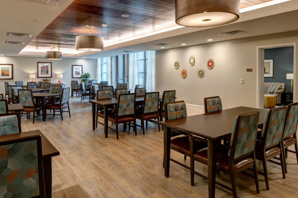 A modern dining area with wooden floors, tables, and chairs under warm lighting.
