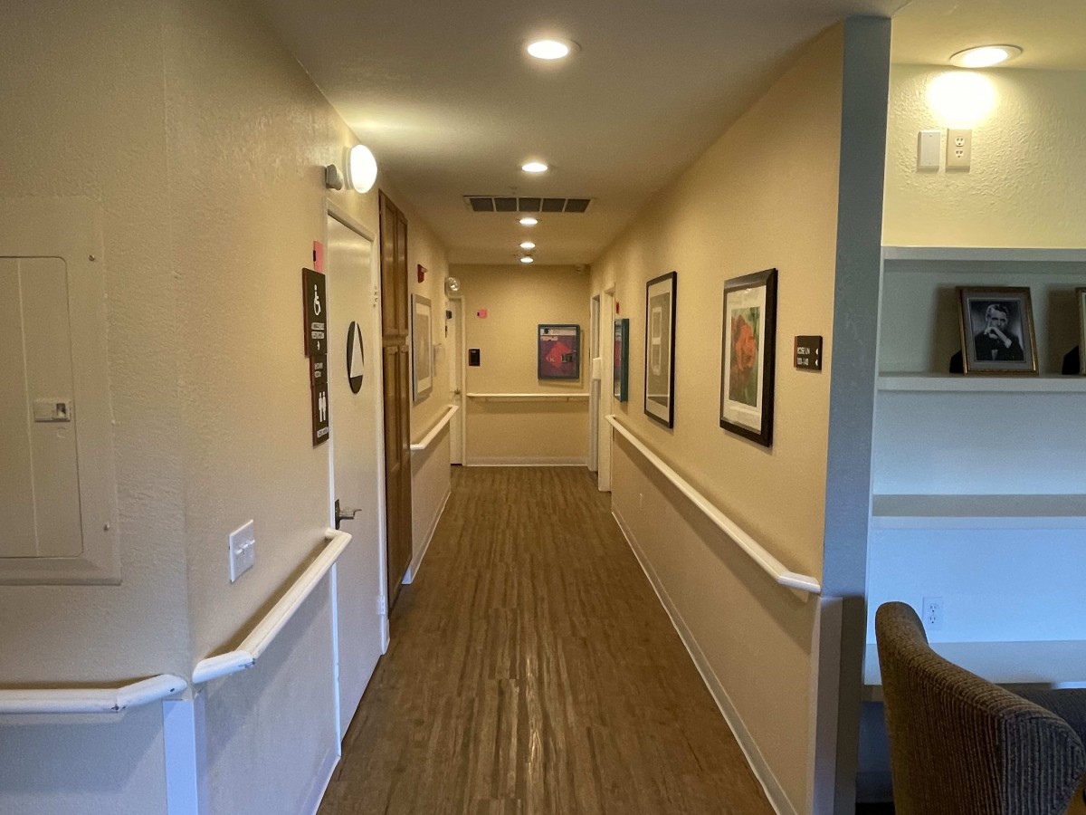 A well-lit hallway with wooden flooring, decorated with framed pictures on the walls.