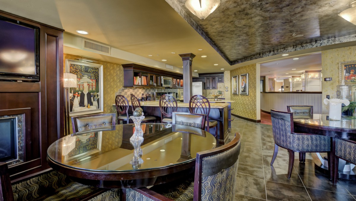 A luxurious dining room featuring a polished table and a stylish bar area, adorned with artwork on the walls.