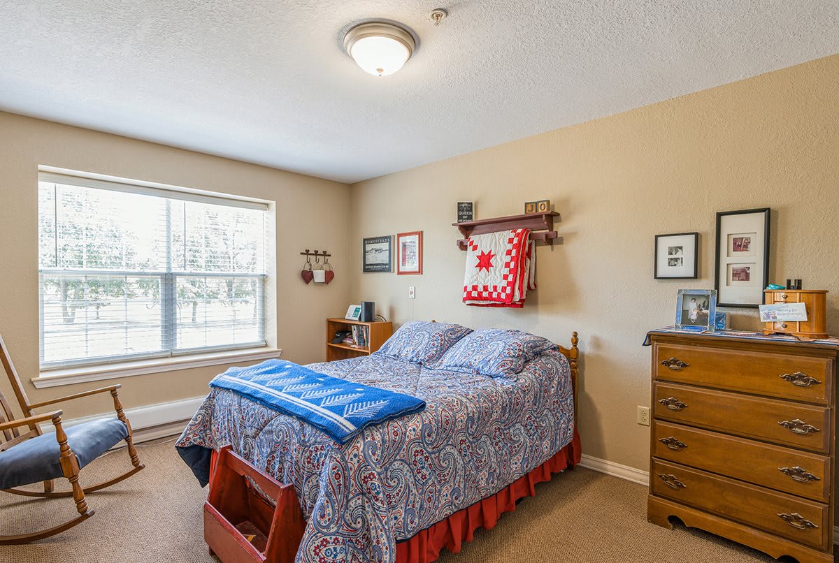 A cozy bedroom with a quilted bed, wooden dresser, and decorative wall items.