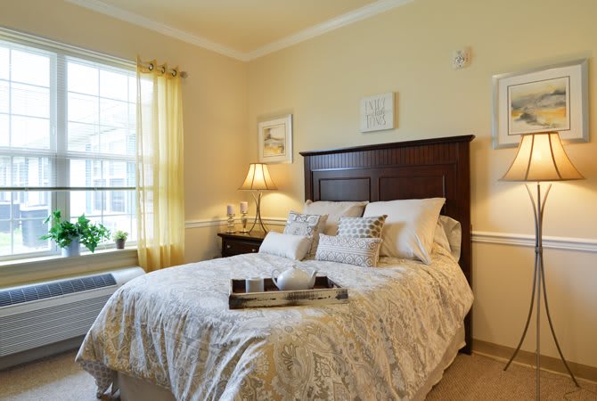 A cozy bedroom with soft lighting, featuring a neatly made bed and a window with yellow curtains.