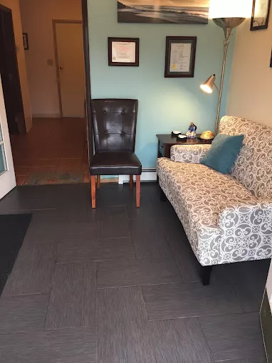 A cozy waiting area with a patterned sofa and leather chair beside a small lamp.