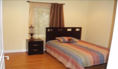 A cozy bedroom with a colorful striped bedspread, a nightstand with a lamp, and wooden floors.