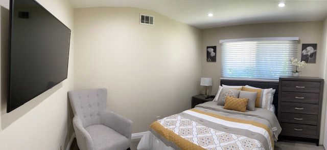 A cozy bedroom with modern decor, featuring a bed, a gray armchair, and a table lamp near the window.