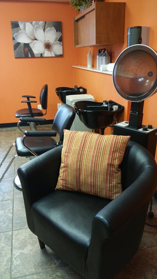 A cozy salon interior featuring chairs, a hairdryer, and washing sinks against an orange wall.