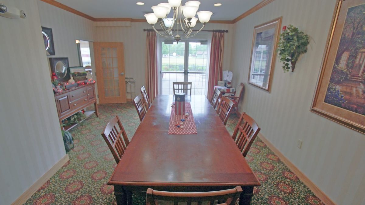 A spacious dining room with a long wooden table and matching chairs, illuminated by a chandelier.