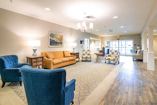 A cozy living room featuring a mix of comfortable seating including a sofa and armchairs, with artwork on the walls and lamps providing ambient lighting.