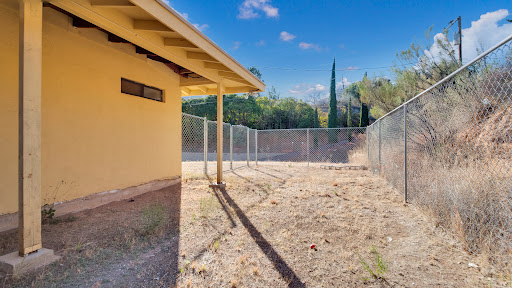 A fenced outdoor area adjacent to a yellow building, featuring dry grass and a clear blue sky.