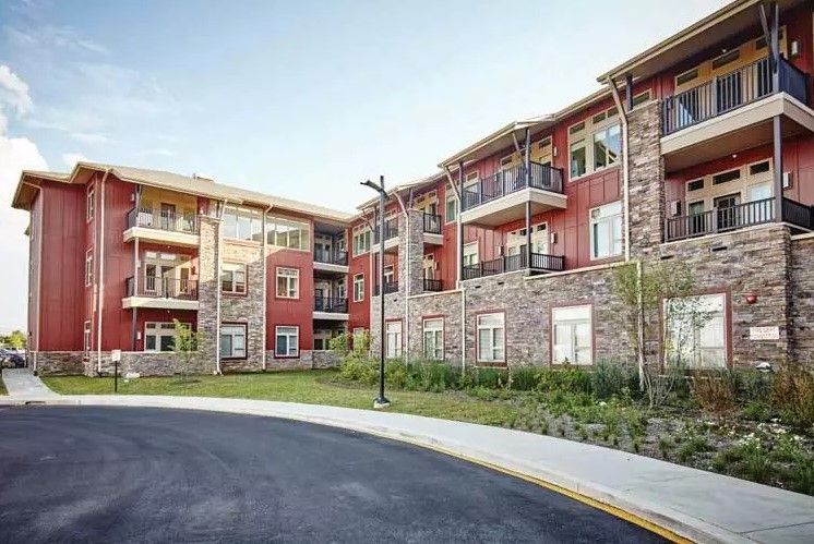 A modern apartment building with stone facades and balconies, surrounded by landscaped areas.