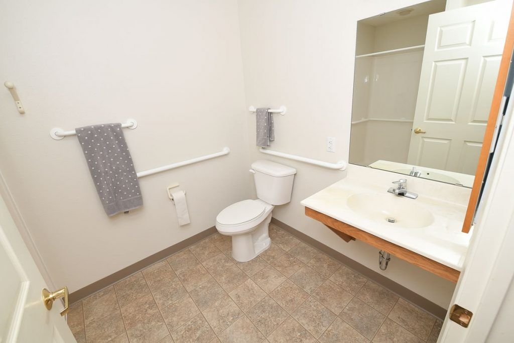 A simple, accessible bathroom with a toilet, sink, and mirror.