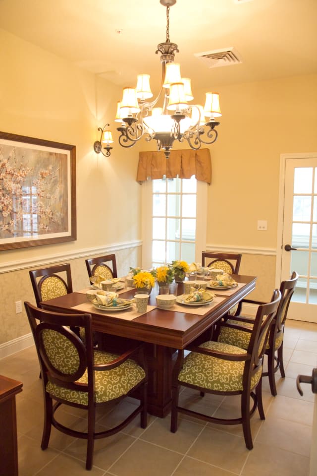 A cozy dining room with a wooden table set for six, featuring elegant decor and a chandelier.