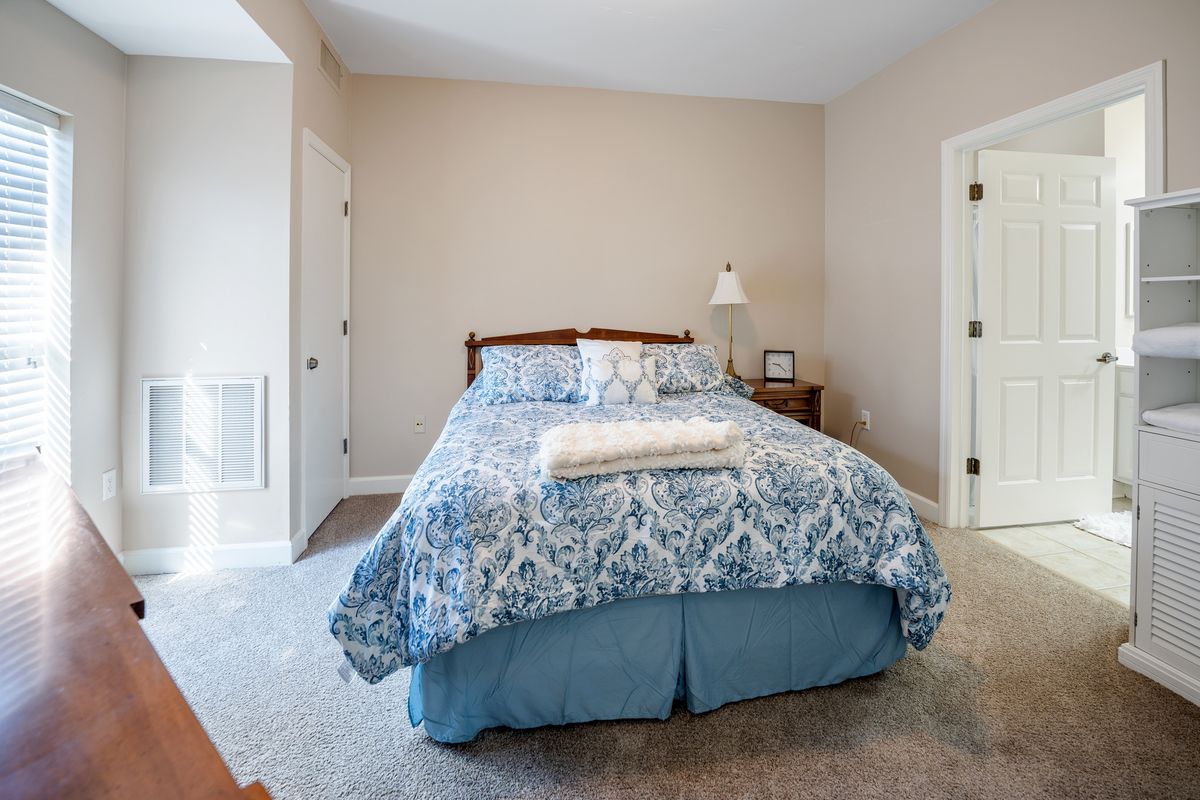A cozy bedroom with a neatly made bed, nightstand, and lamp.