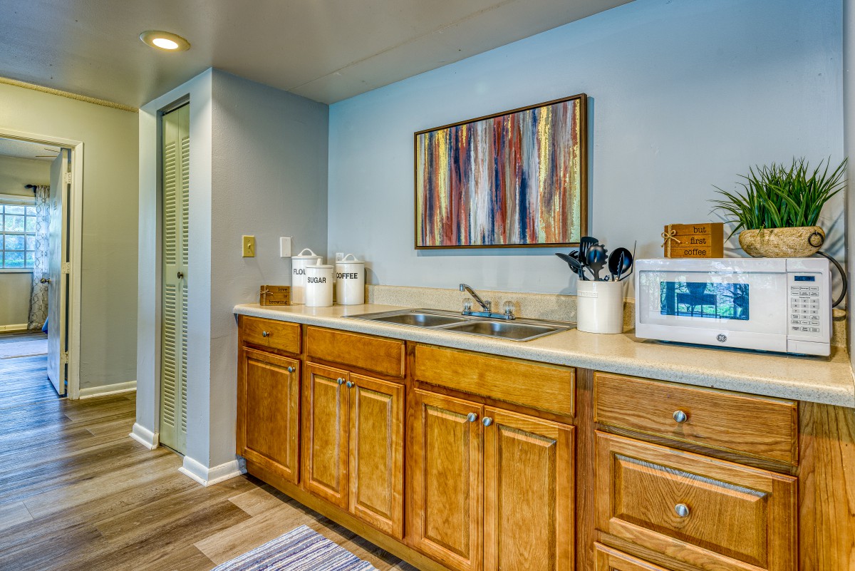 A cozy kitchen with wooden cabinets, a sink, countertop appliances, and colorful artwork on the wall.