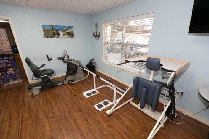 A well-lit exercise room with various gym equipment, including a stationary bike and other fitness machines, on a wooden floor.