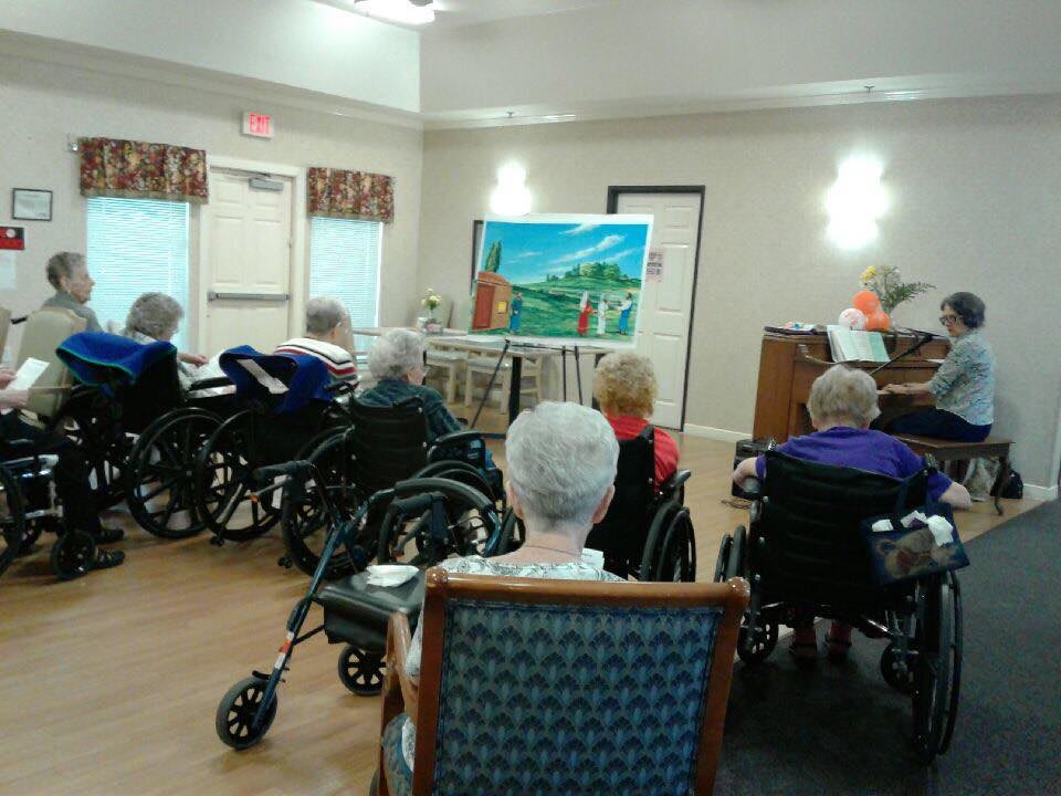 A group of elderly people in wheelchairs participates in a painting class at a nursing home.