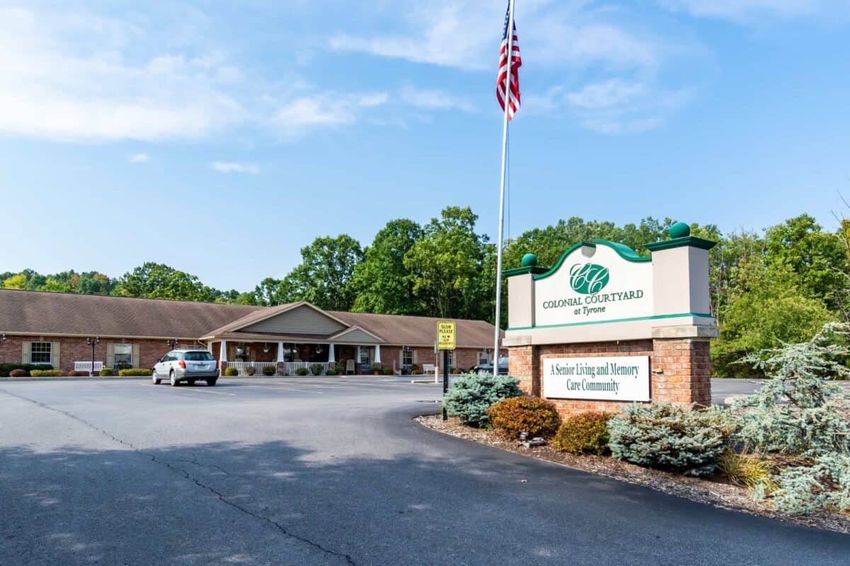 A building with a signboard in front, surrounded by a parking lot and trees, under a clear sky.