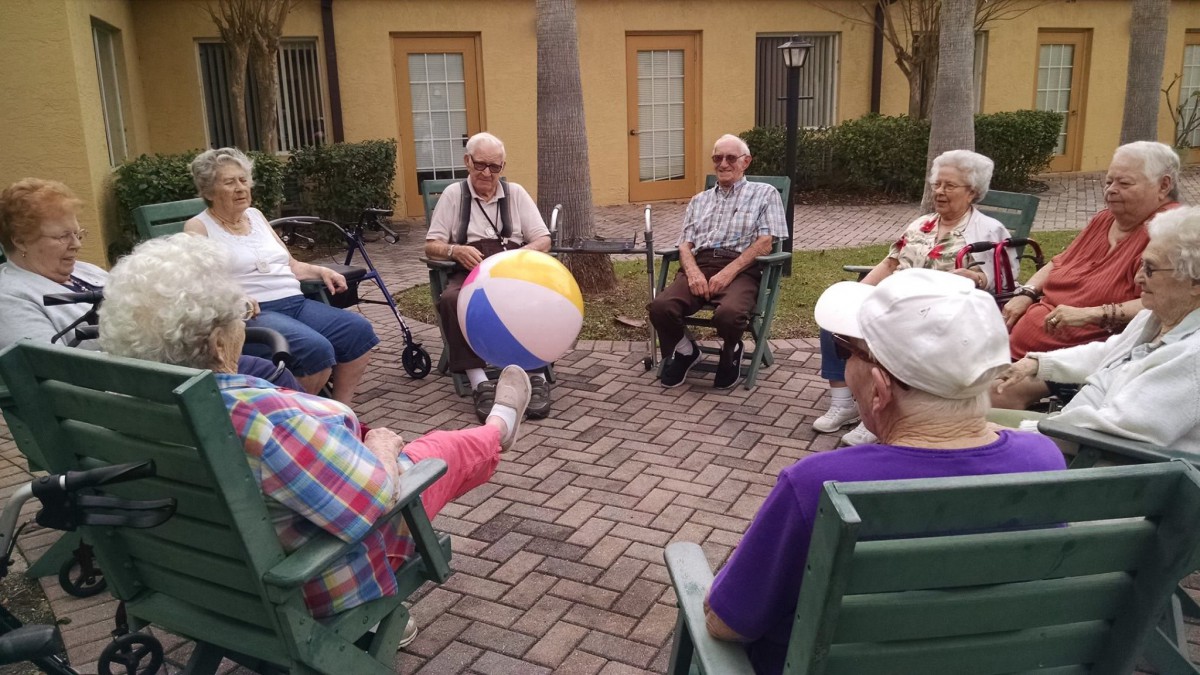 A group of seniors enjoying an outdoor activity with a beach ball while seated in a circle.
