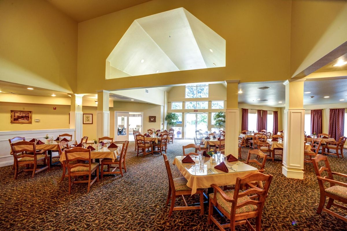 An elegant restaurant dining area with neatly arranged tables and chairs, featuring large windows and a patterned carpet.