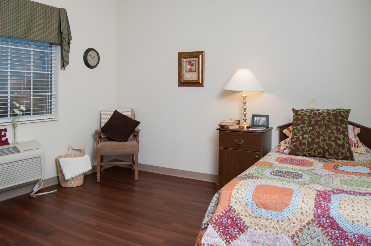 A cozy bedroom with a quilt-covered bed, wooden dresser, and decorative elements on the wall.