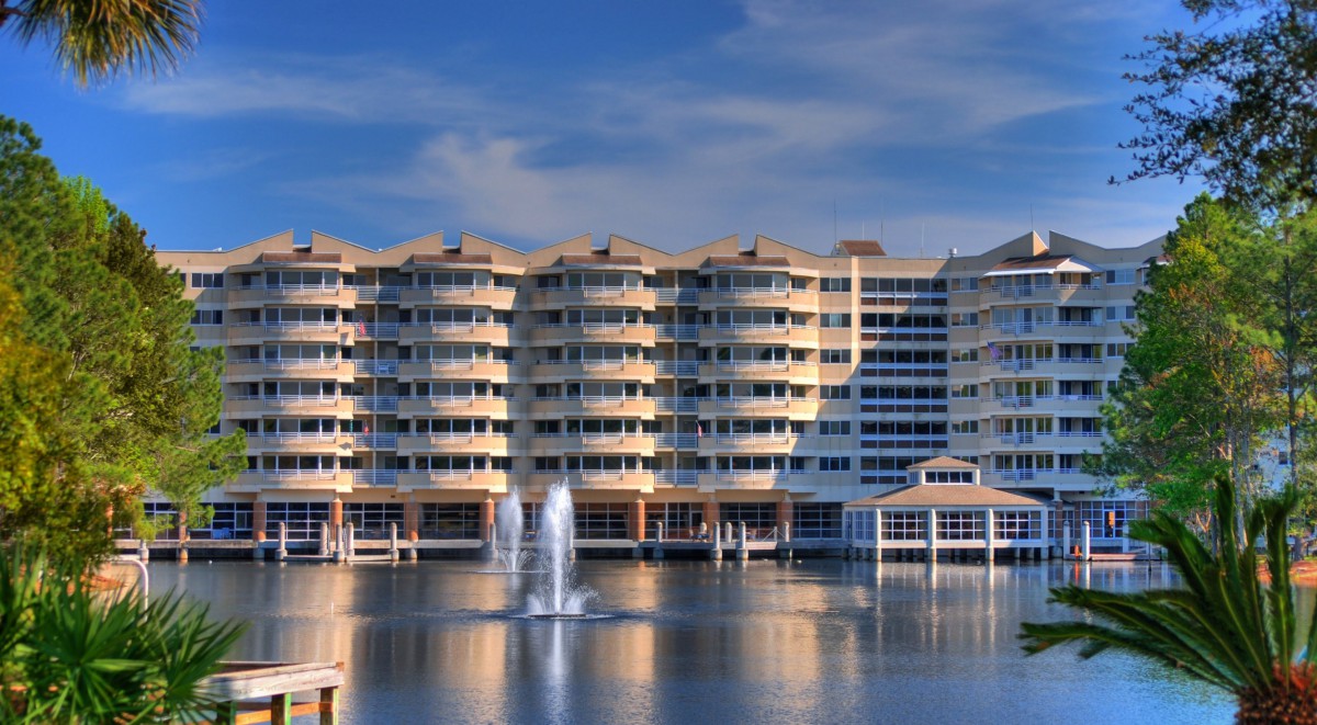 A large waterfront residential building with multiple balconies and a fountain in front.