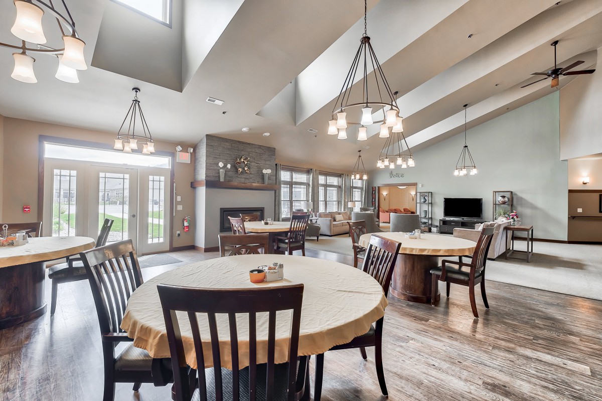 A spacious and modern community dining area with multiple tables, chairs, and chandeliers.