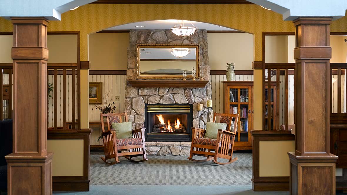 A cozy living room with a stone fireplace, two wooden rocking chairs, and a bookshelf.