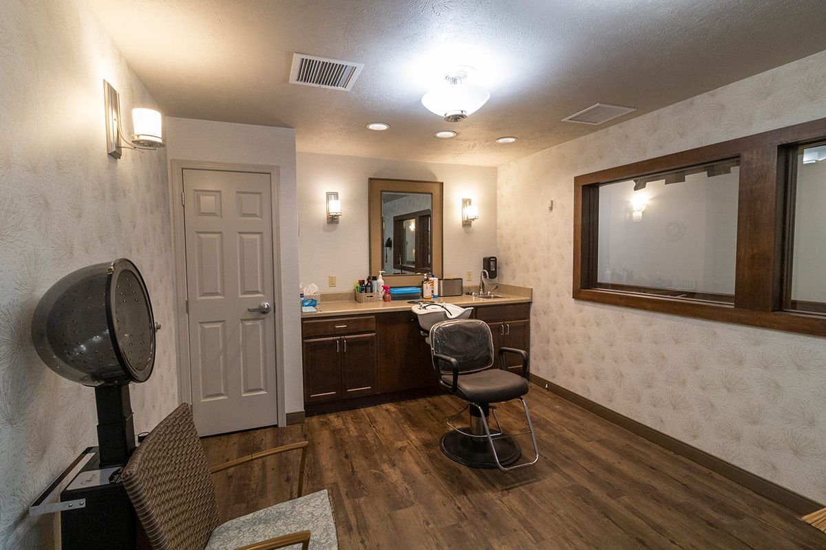 A modern salon room featuring a hairdressing chair, mirror, and sink.