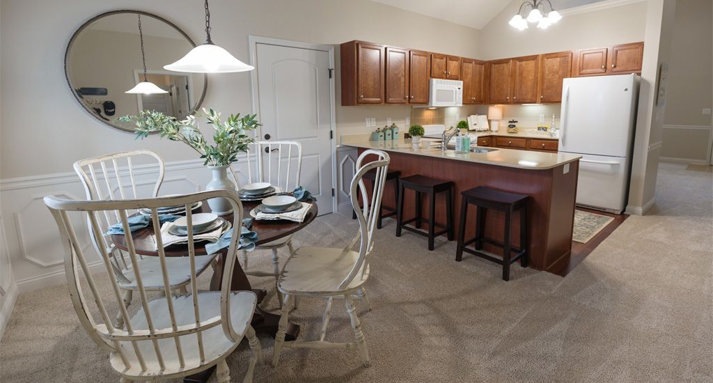 A cozy kitchen and dining area featuring wooden cabinets, a glass-top table with chairs, and bar stools along the countertop.