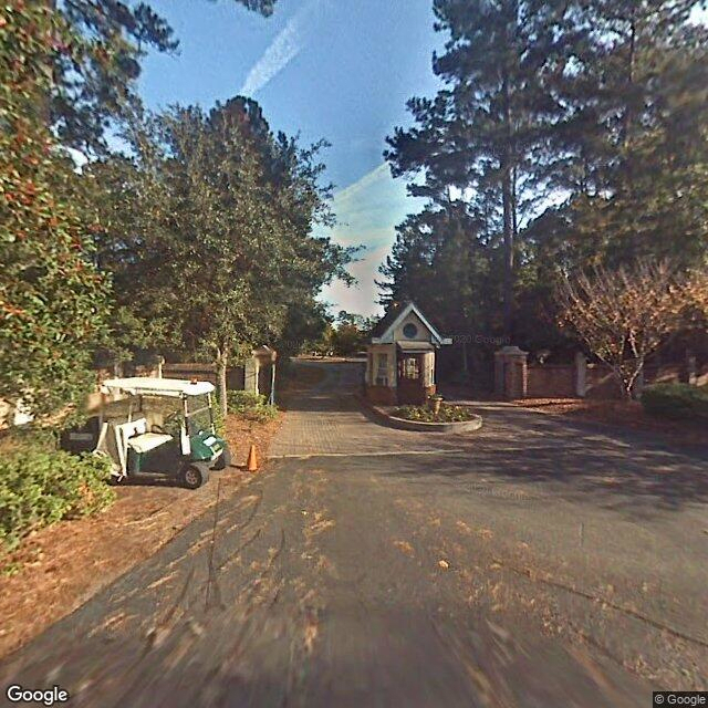 A suburban gated community entrance with a security booth and surrounding trees.