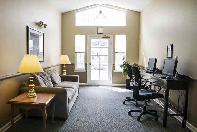 A cozy office space with computers and a sofa, illuminated by natural light from large windows.