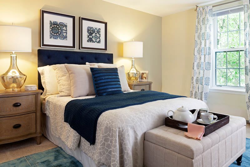 A beautifully decorated modern bedroom featuring a neatly made bed with blue accents and elegant lighting.