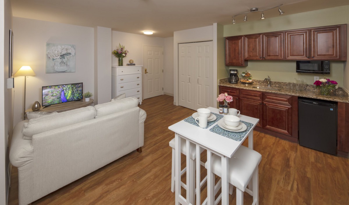 A cozy apartment with an open-plan living room and kitchen, featuring modern furniture and a small dining table.