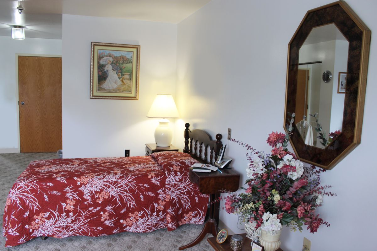 A cozy bedroom with a floral bedspread, a lamp on the bedside table, and decorative flowers near a mirror.