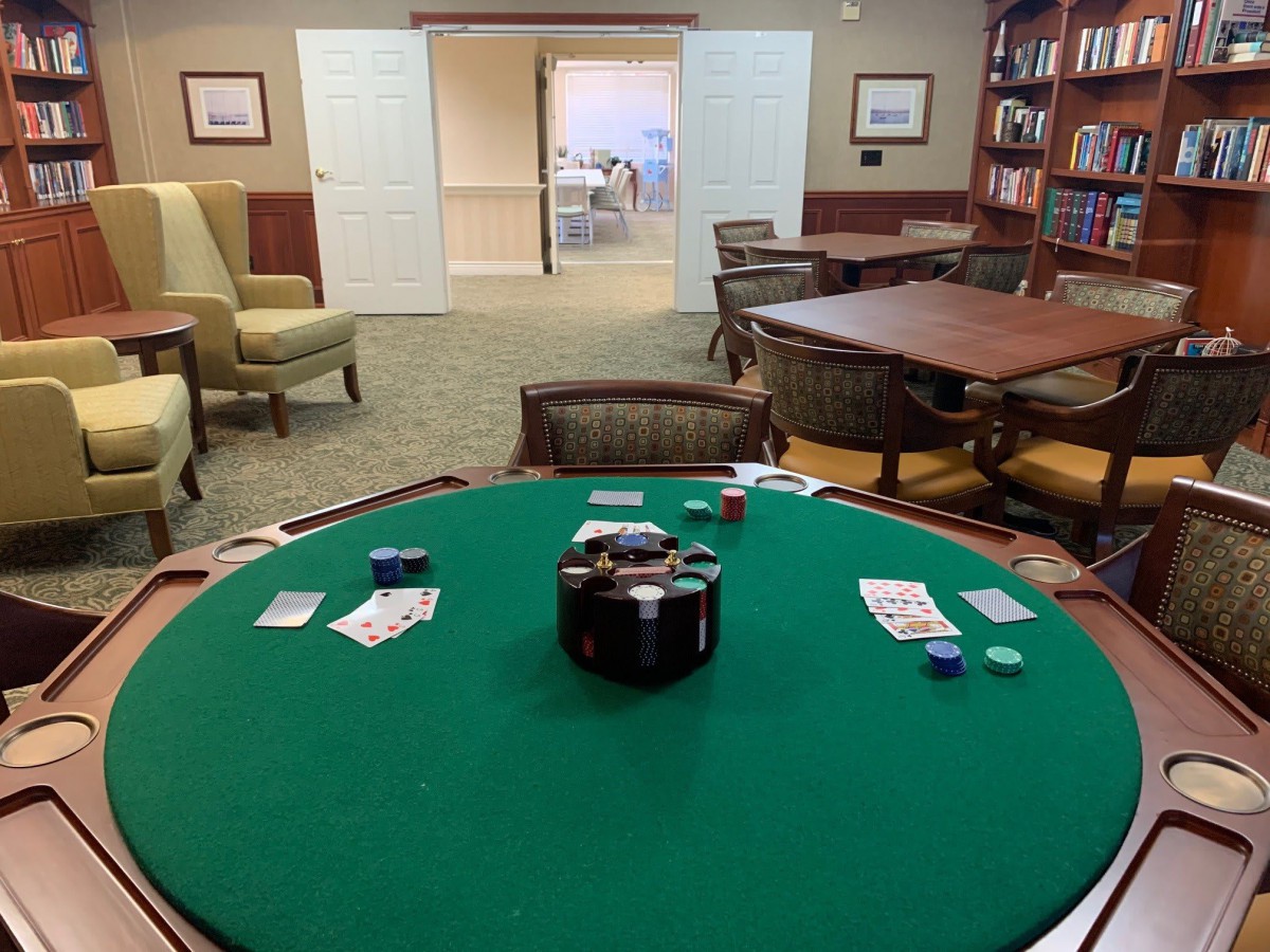 A quiet game room with a poker table set up for play, surrounded by comfortable seating and bookshelves.