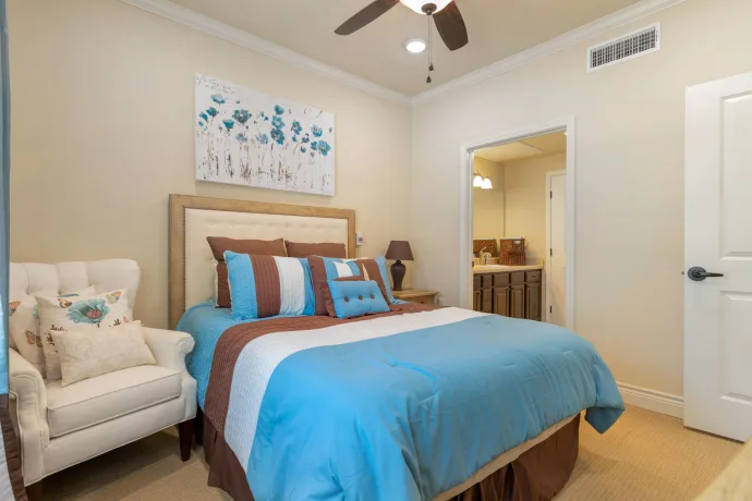 A modern bedroom featuring blue and brown bedding, complemented by a floral artwork and warm lighting.