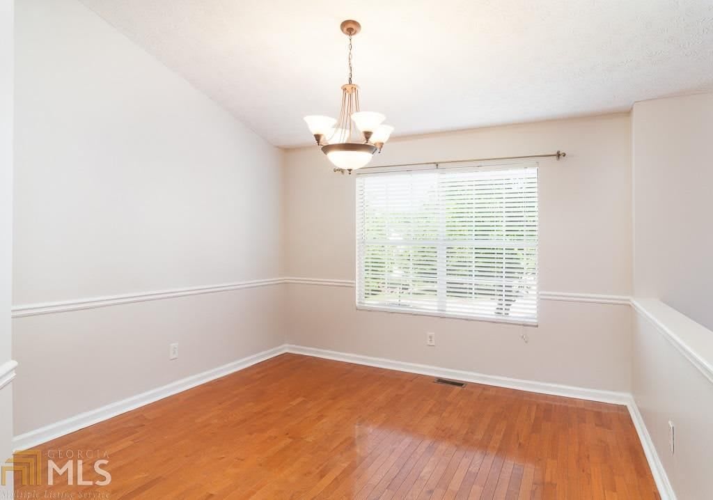 An empty dining room with hardwood floors, a chandelier, and a large window letting in natural light.