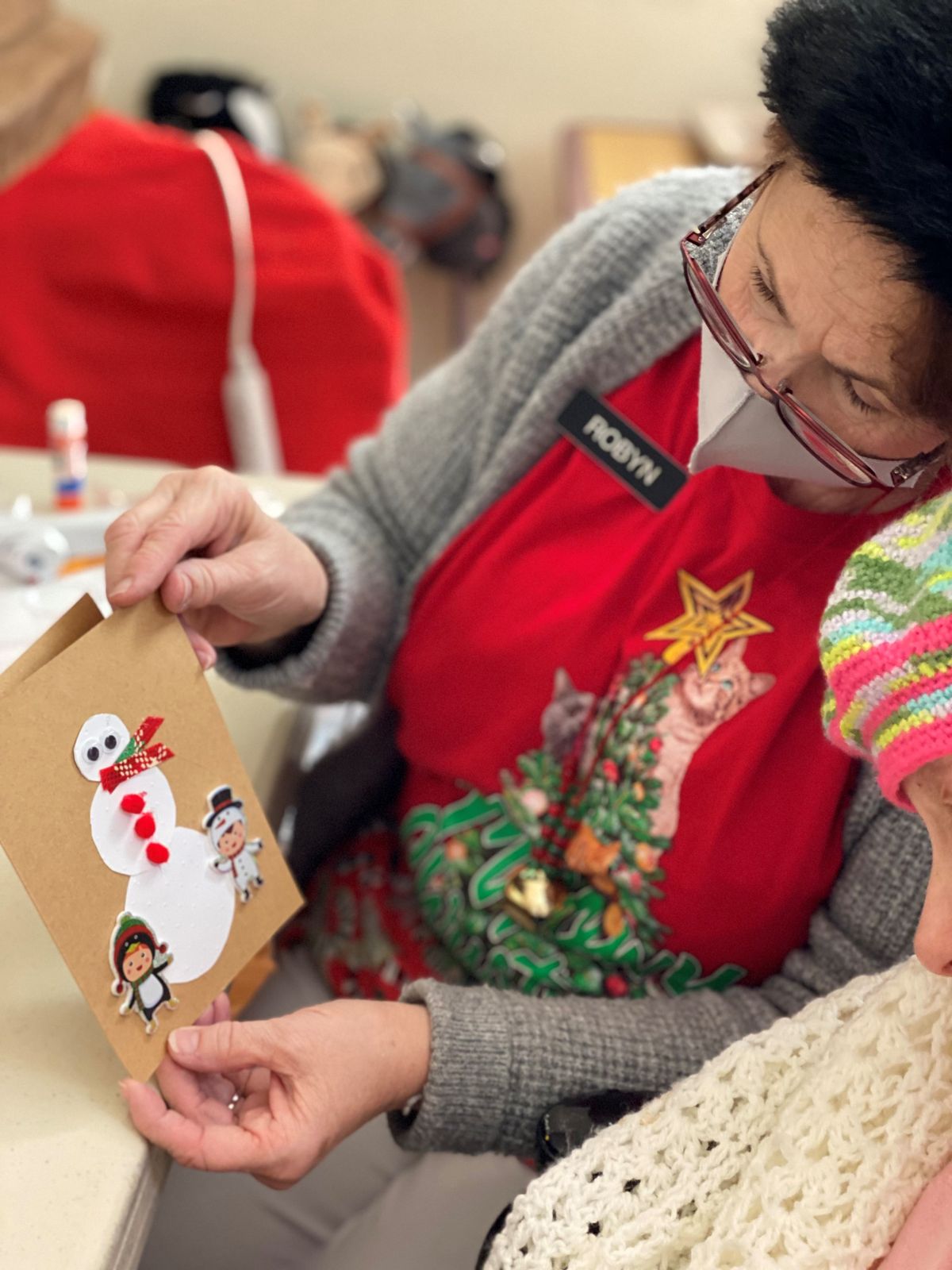A woman and child engage in holiday crafting, making a snowman card.