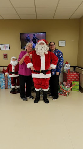 A joyful holiday gathering featuring Santa Claus surrounded by cheerful individuals and wrapped gifts.