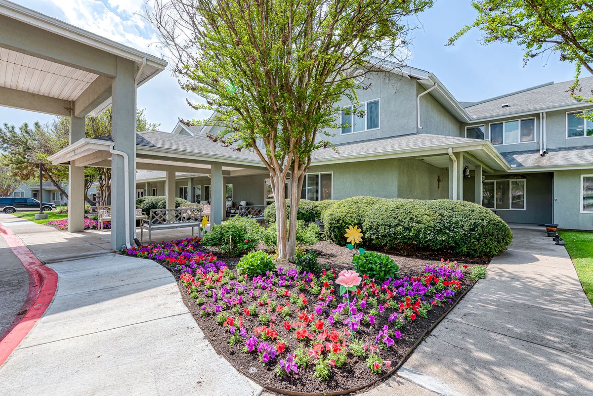 A beautifully landscaped garden with colorful flowers and a tree in front of a house.