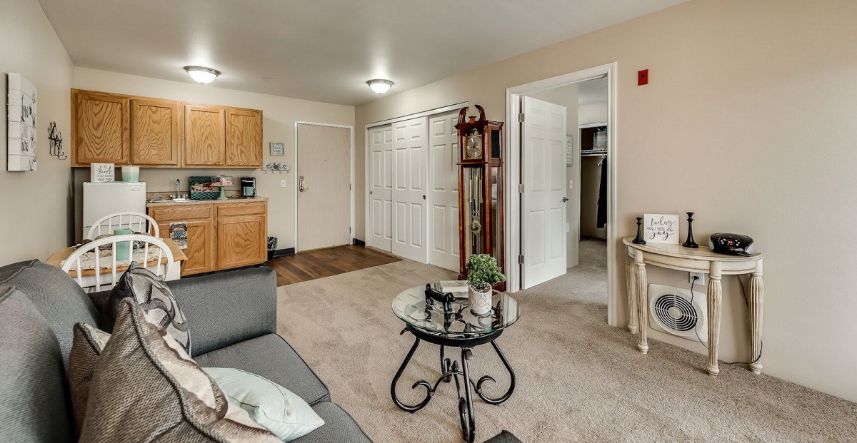 A cozy living room with a sofa, glass coffee table, and an open view to the kitchen area.